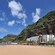 Resort hotel set against a rocky cliff with sandy beach, palm trees and lounge chairs out front